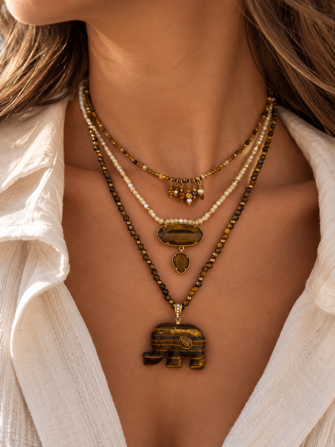 Cou d’une femme portant une composition de collier en acier inoxydable et pierres naturelles dans les tons de marron et blanc cassé 