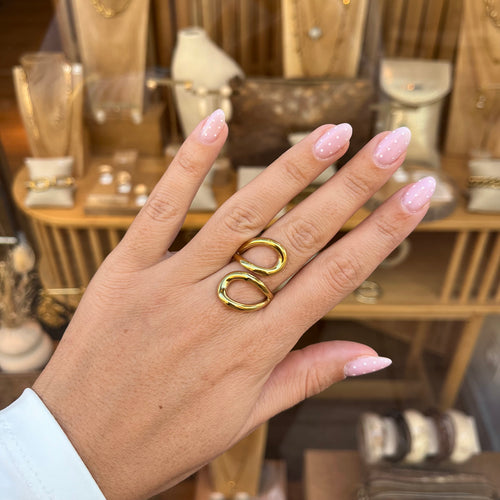 Main d’une femme portant une bague réglable en acier inoxydable doré, avec deux anneaux qui se croisent sur le dessus 