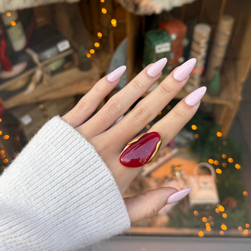 Main de femme portant une bague en acier inoxydable doré, serti d une pierre ovale rouge en résine 