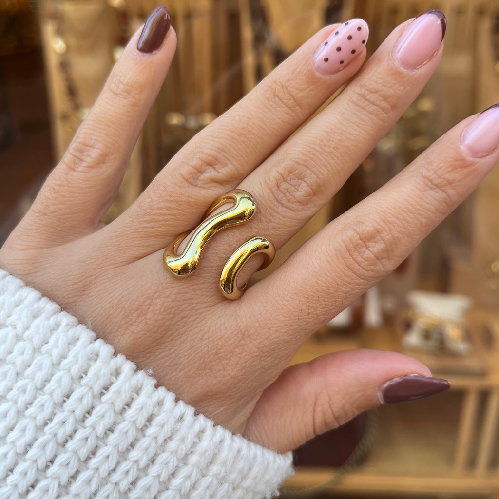 Main avec une bague en acier inoxydable doré, ayant une forme géométrique et ouverte sur le dessus