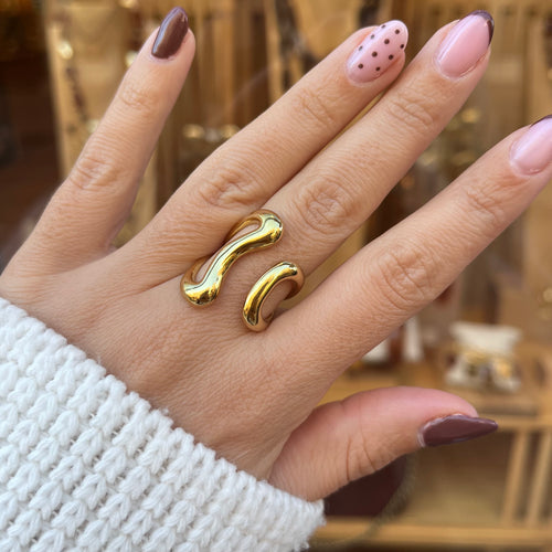 Main avec une bague en acier inoxydable doré, ayant une forme géométrique et ouverte sur le dessus
