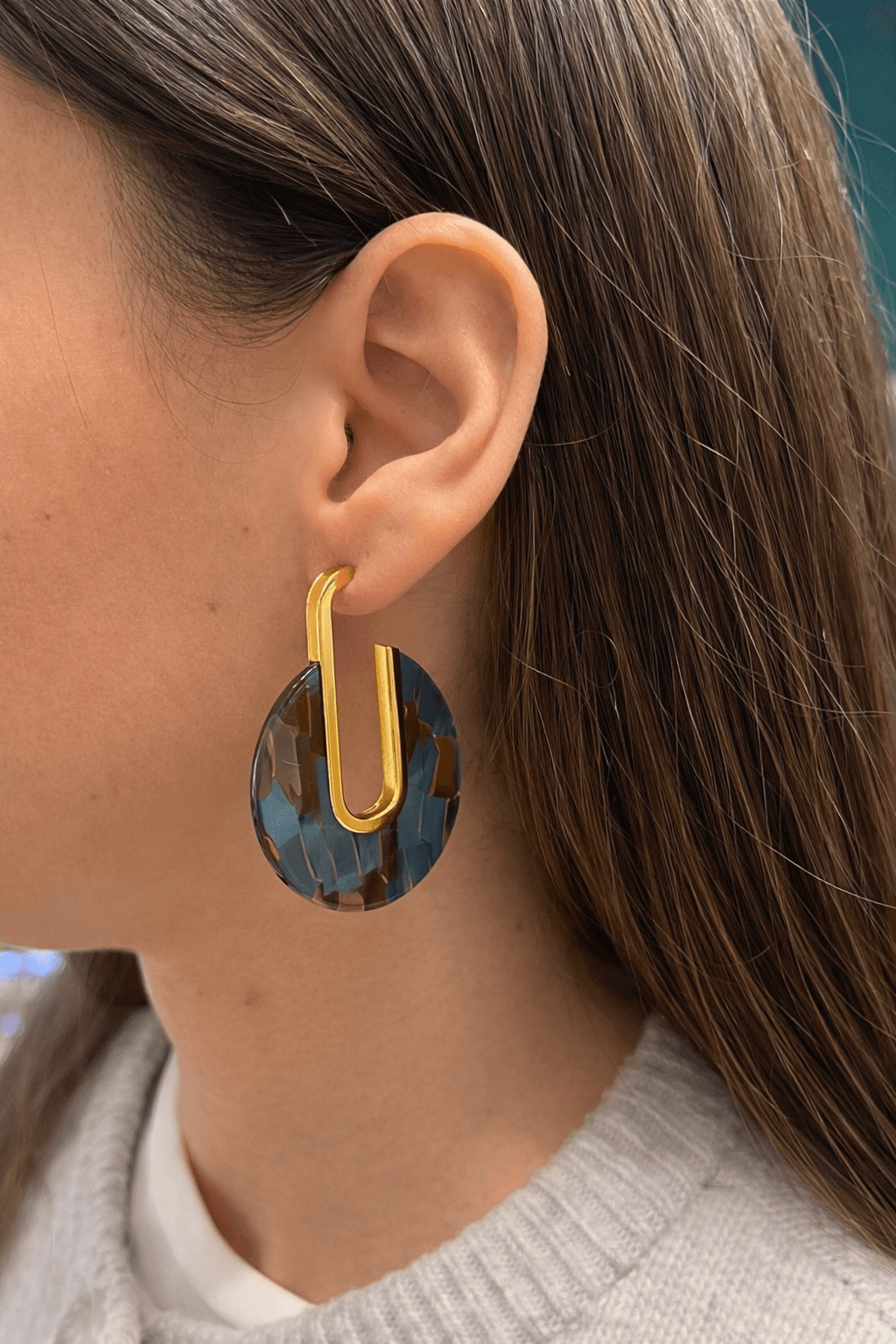 Femme portant une paire de boucles d’oreilles en acier inoxydable doré et en résine 