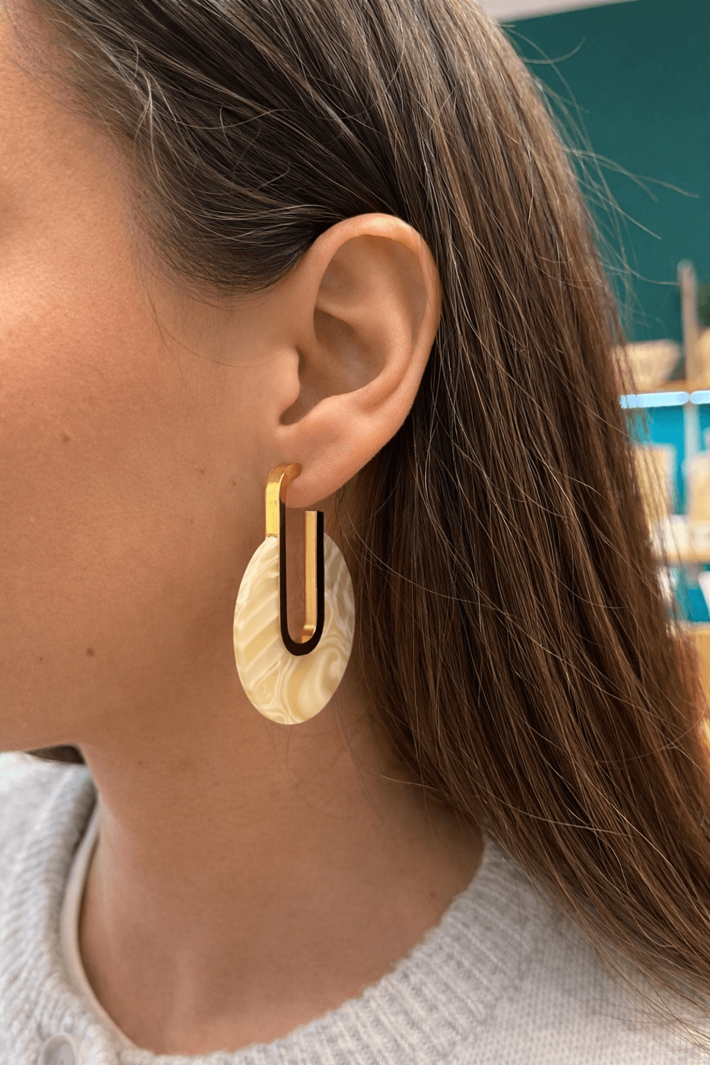 Femme portant une paire de boucles d’oreilles pendantes en acier inoxydable doré et en résine, marbré beige 
