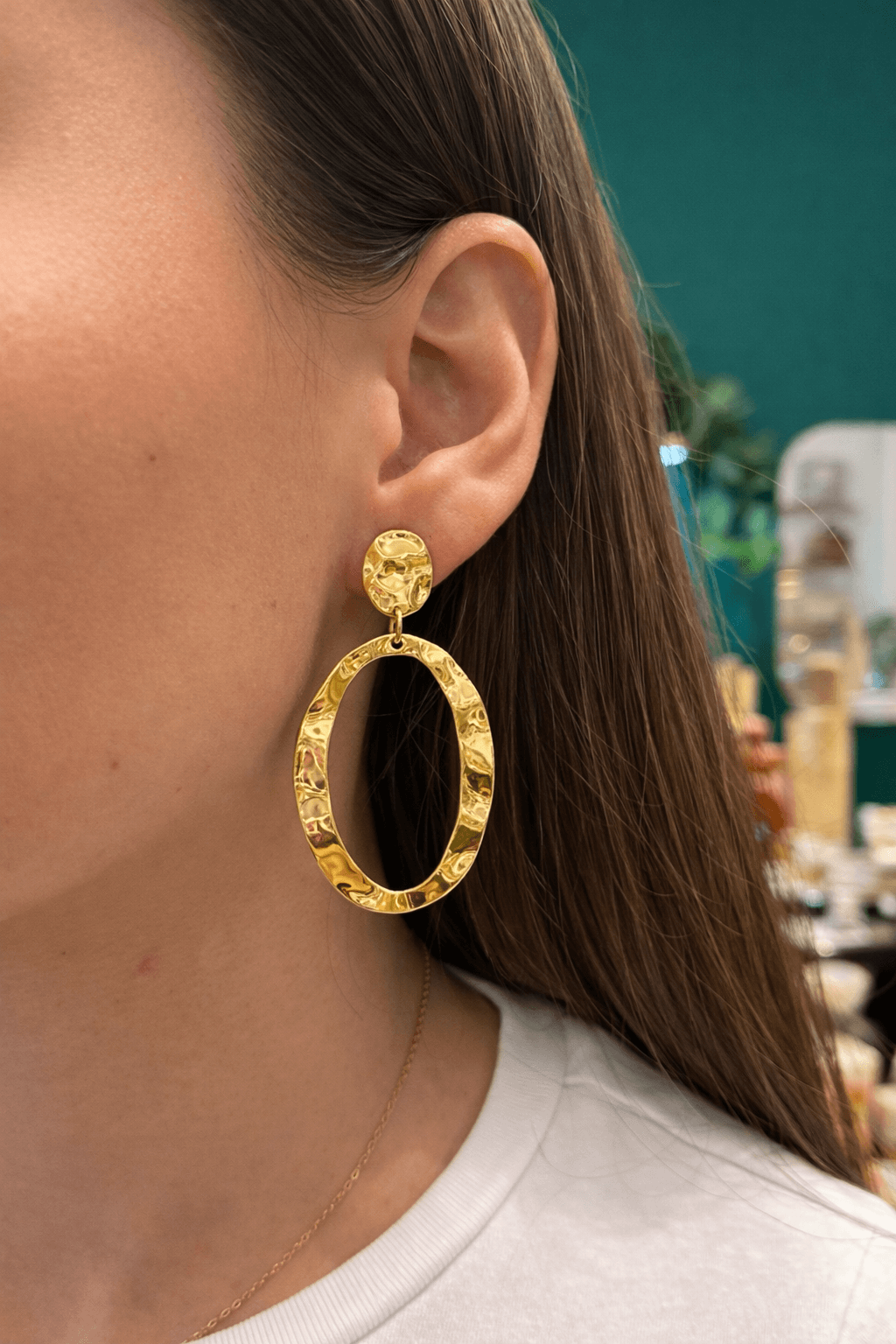 Femme portant une paire de boucles d’oreilles pendantes avec un anneau martelé et ouvert au centre, en acier inoxydable doré