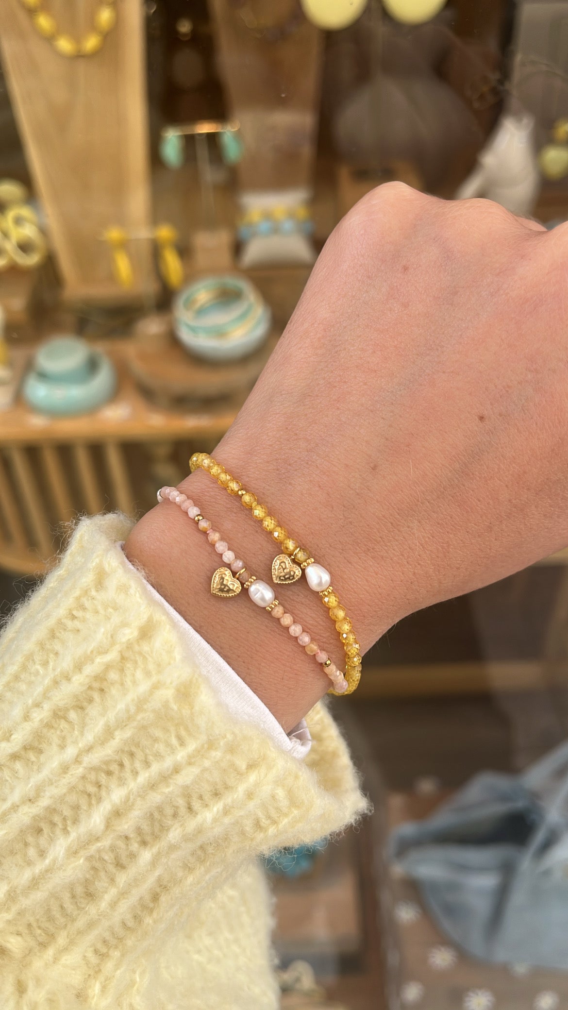 Poignet de femme portant 2 bracelets à perles de couleurs avec un coeur en acier inoxydable doré