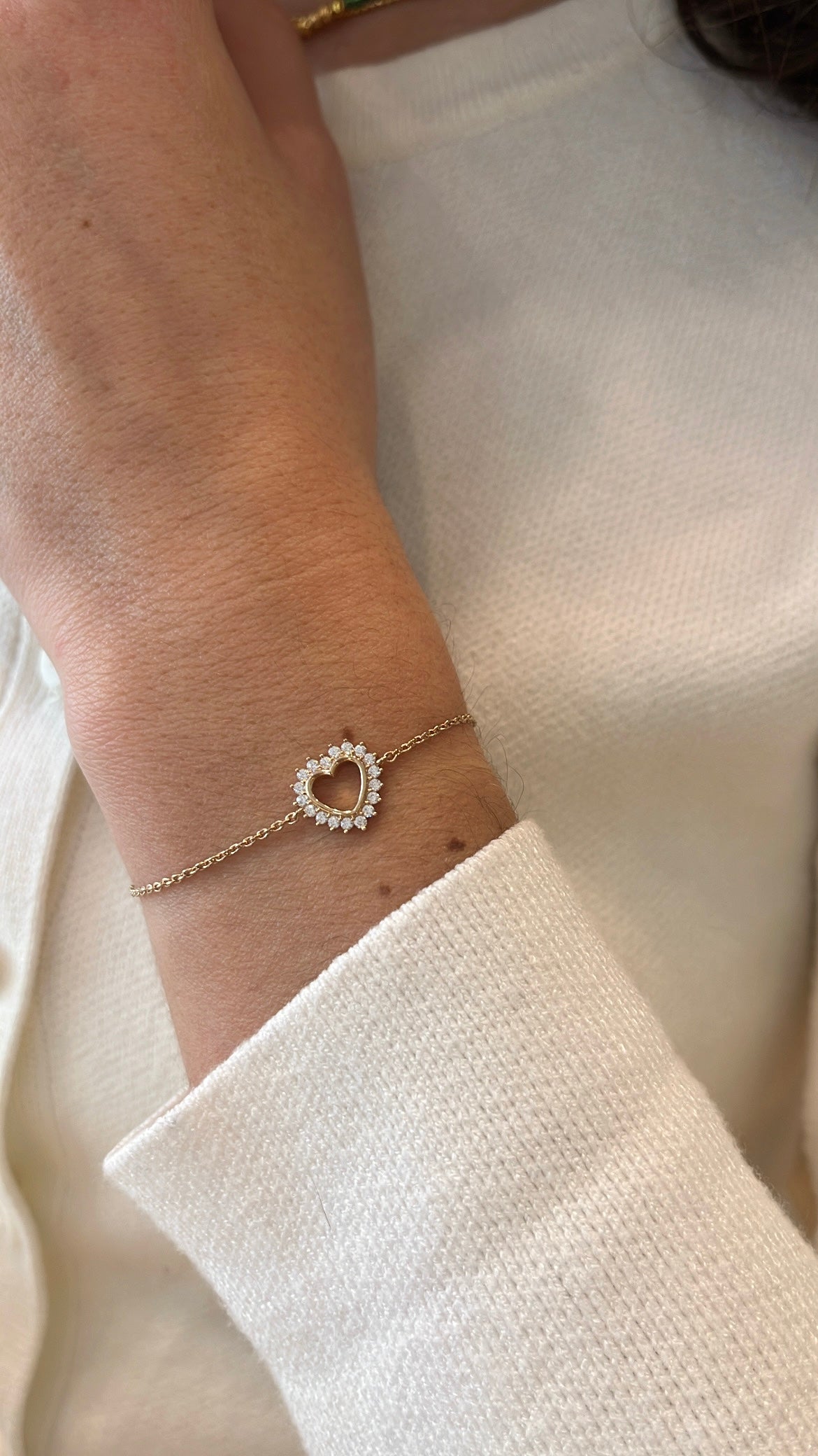 Poignet portant un bracelet en plaqué or, avec un cœur entouré de zircons