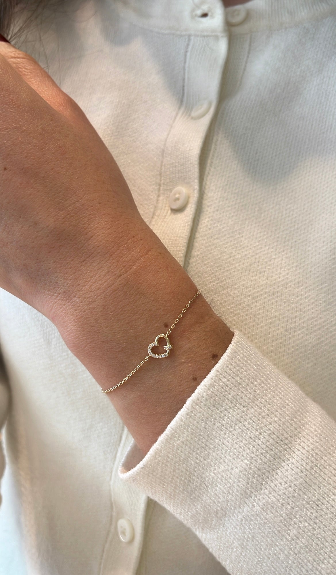 Poignet d’une femme portant un bracelet avec un cœur, en plaqué or et zircons 
