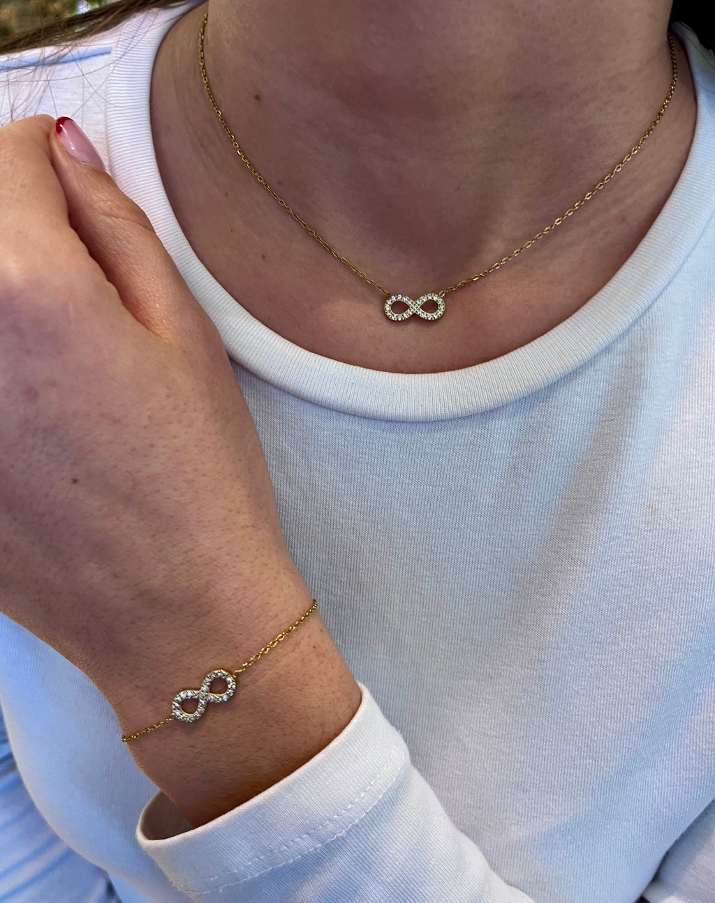 Parure collier bracelet en acier inoxydable doré à ce le signe de l’infini, portées par une femme