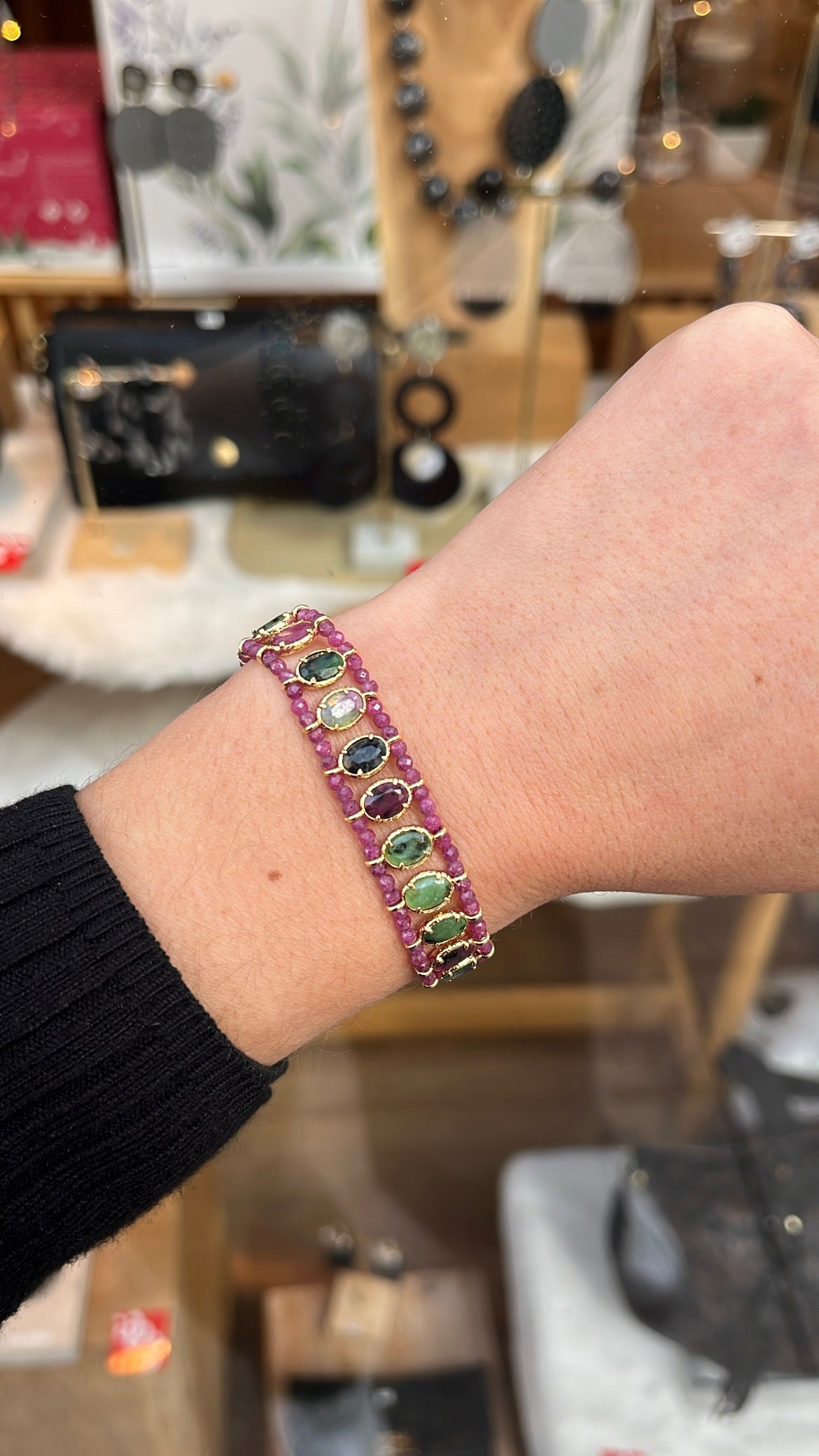 Poignet de femme portant un bracelet avec des pierres naturelles rose et vertes, serties sur de l’acier inoxydable doré