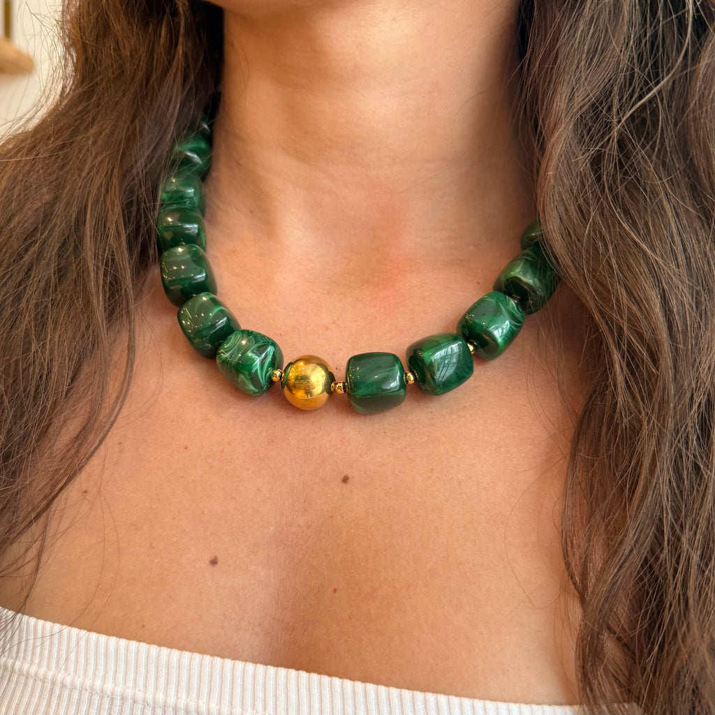 Cou d’une femme portant un collier en résine vert, avec une perle en acier inoxydable doré au centre du collier 