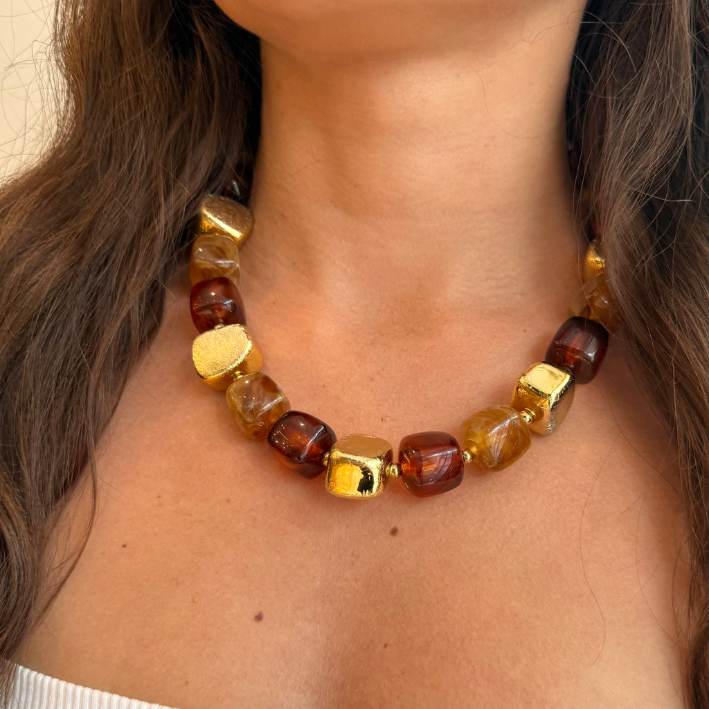 Collier en perles de résine, de couleur marron et doré, porté par une femme