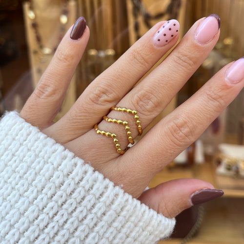 Main portant une bague en acier inoxydable doré, que a 3 traits avec des petites boules sur le dessus 