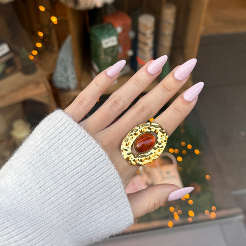 Main de femme portant une bague en acier inoxydable doré, style martelé a ce une pierre ovale marron sur le dessus