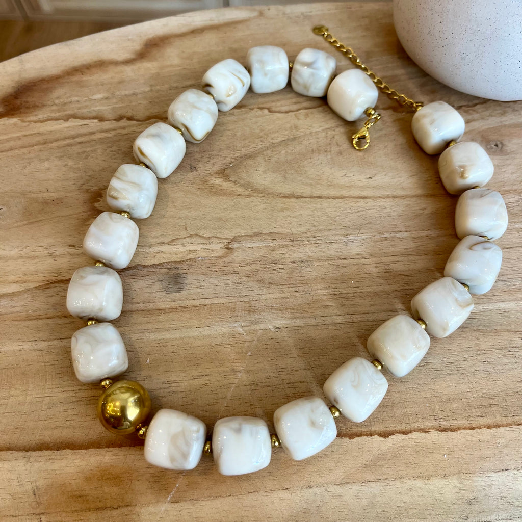 Collier femme avec des perles carrées en résine de couleur blanc cassé, ainsi qu’une perle en acier inoxydable doré au milieu 