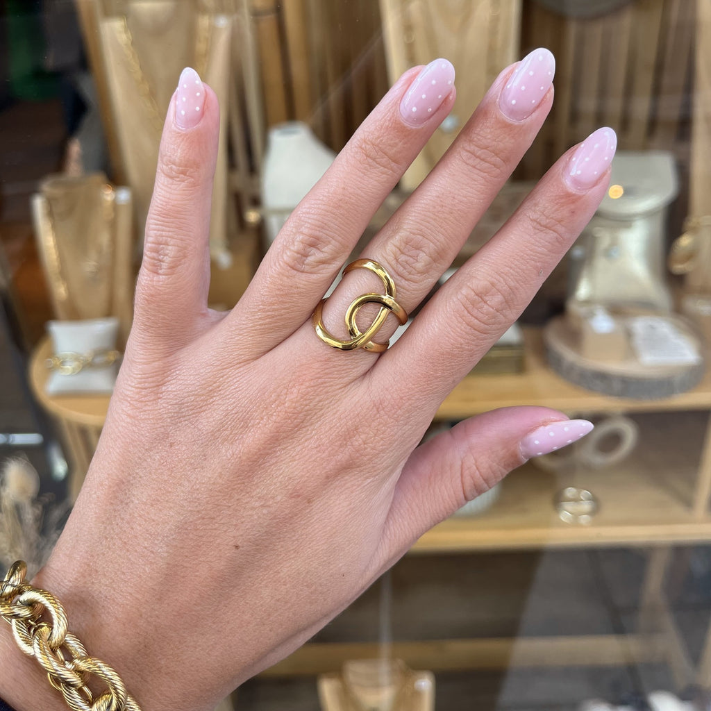 Main d’une femme portant une bague réglable en acier inoxydable doré avec 2 boucles qui se croisent 