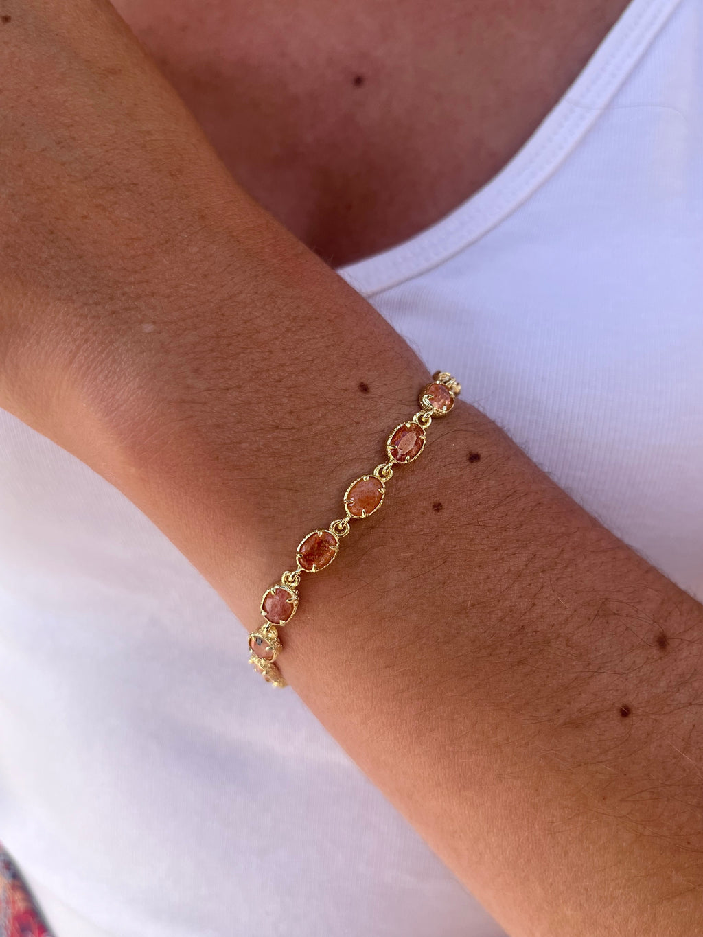 poignet de femme portant un bracelet en acier inoxydable doré et en pierres naturelles coraline