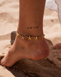 pieds d'une femme portant une chaine de cheville avec des étoiles de mer en acier inoxydable doré
