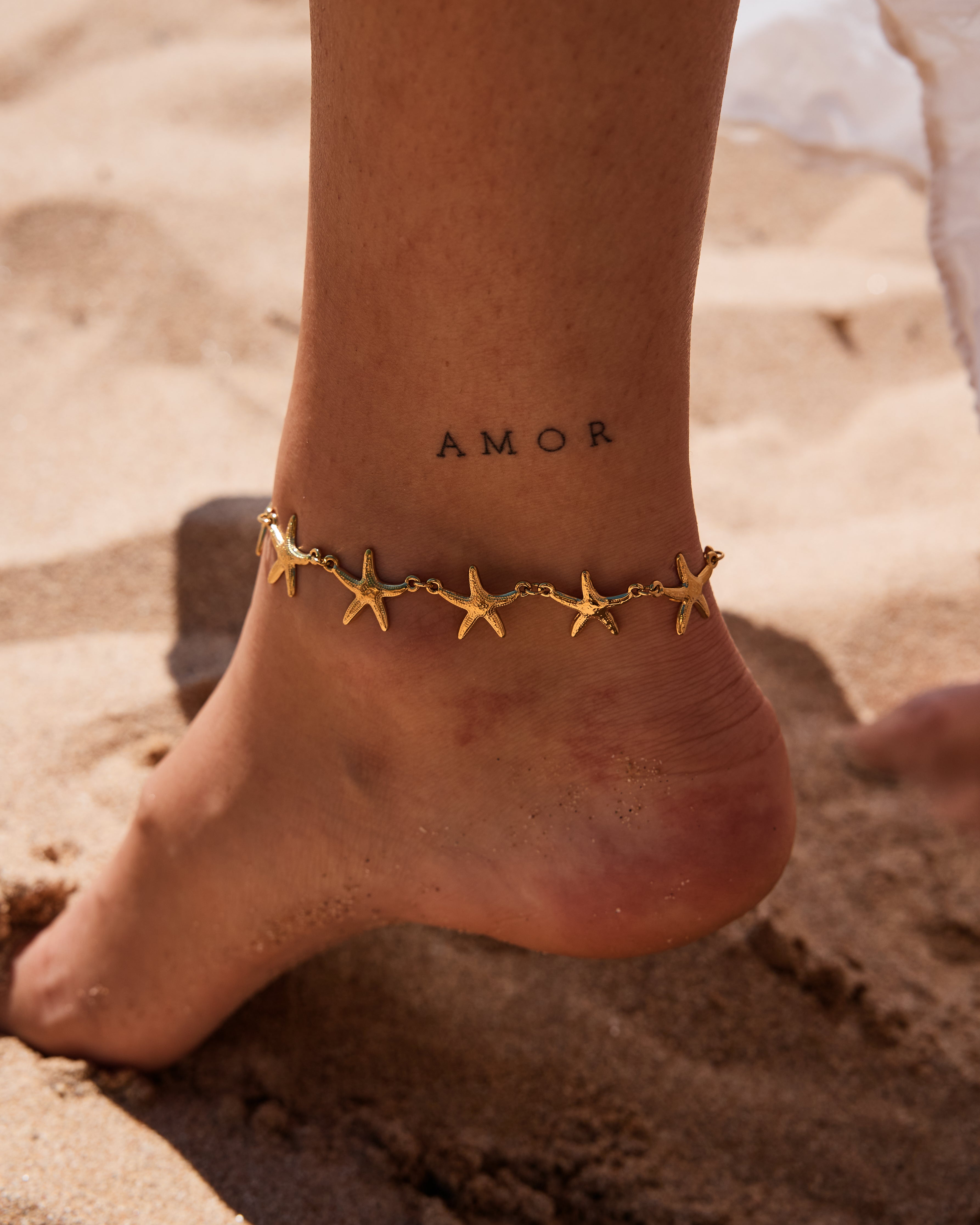pieds d'une femme portant une chaine de cheville avec des étoiles de mer en acier inoxydable doré
