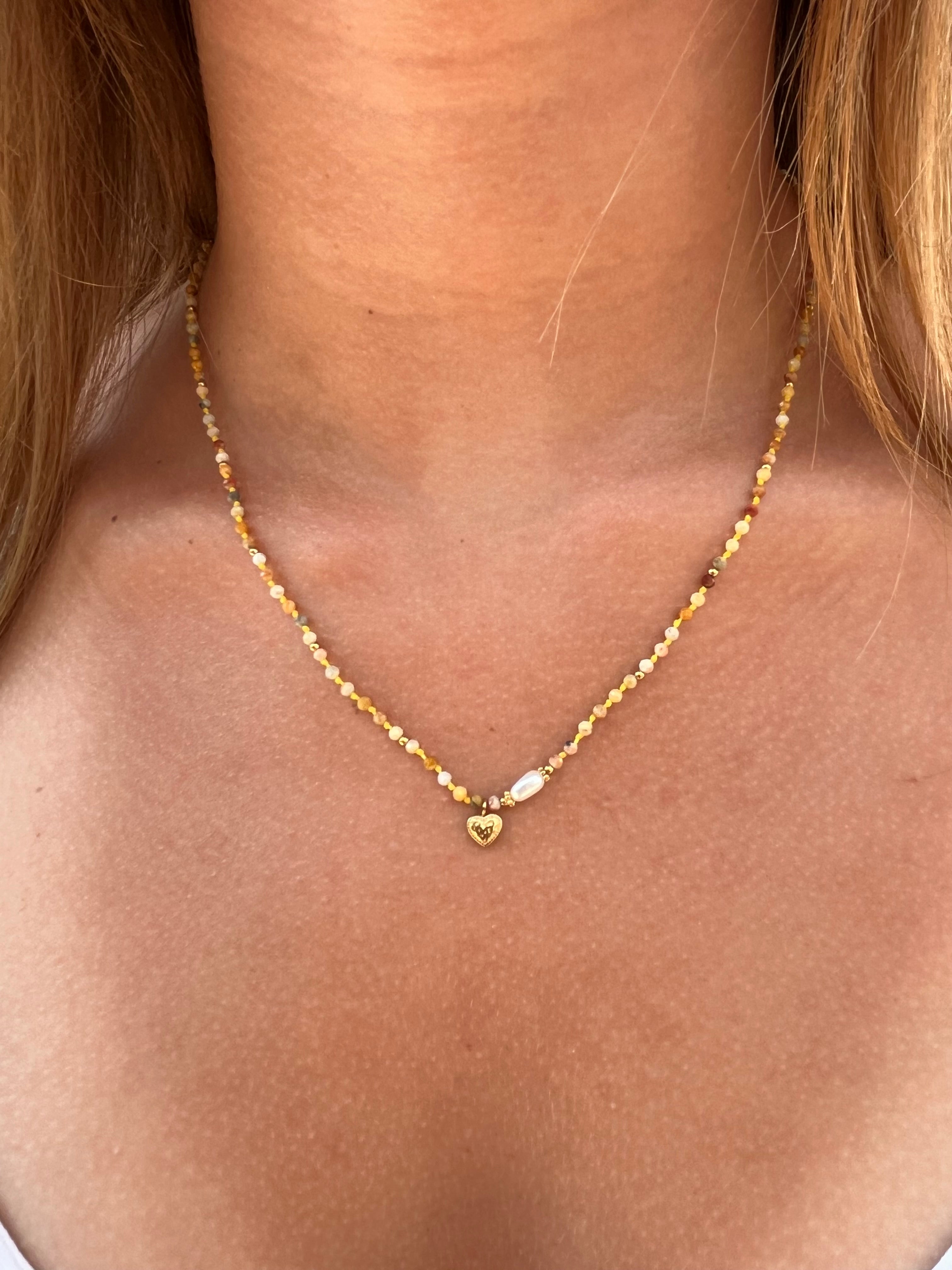 cou d'une femme portant un collier de pierres naturelles jaune avec un petit coeur en acier inoxydable doré et une perle blanche