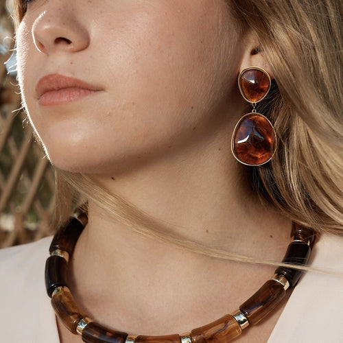 Boucles d’oreilles pendantes en pierres marrons serties sur de l’acier inoxydable doré, portées par une femme